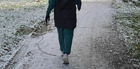 henkilö kävelee hieman lumisella kävelytiellä